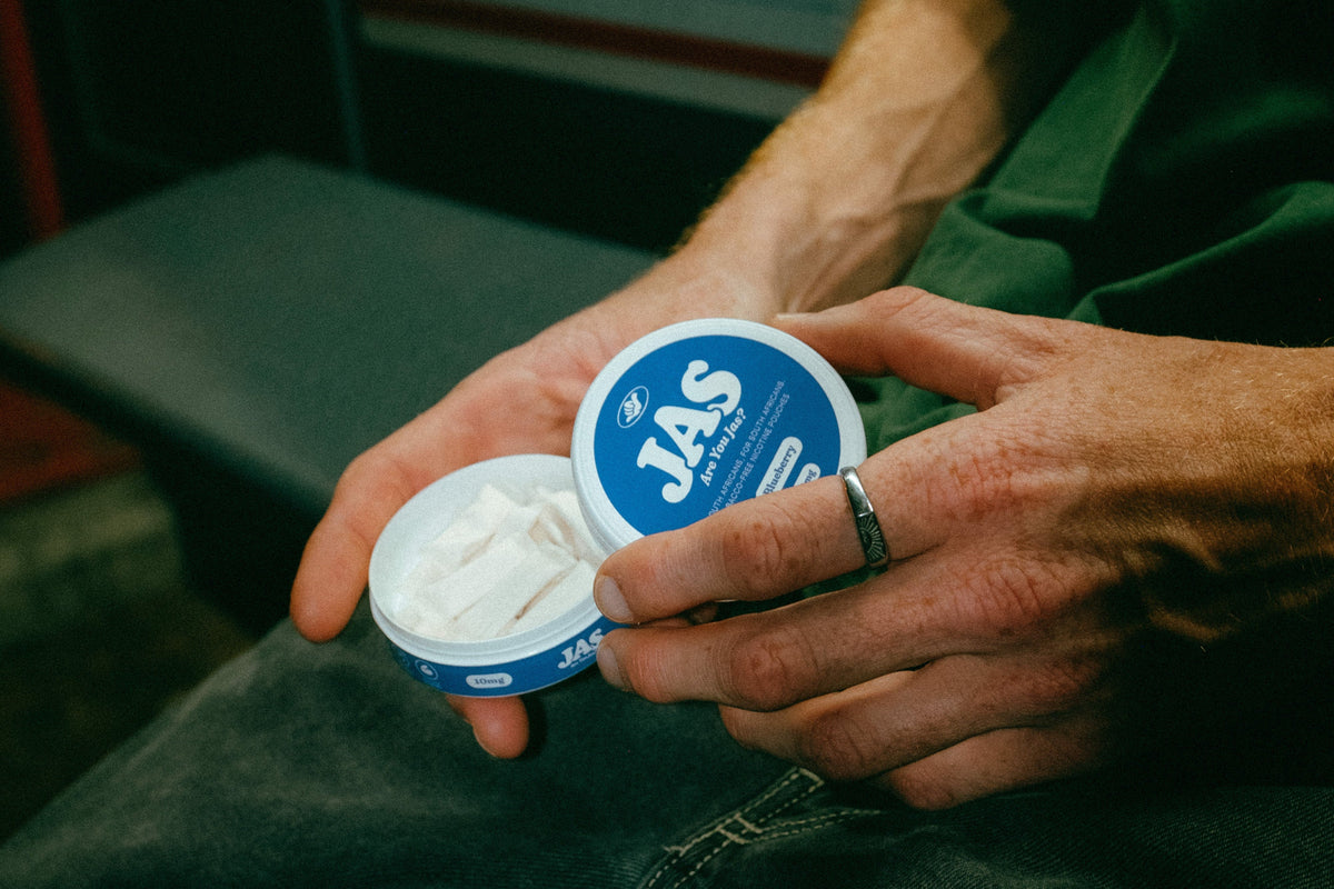 Person holding two containers of JAS brand product in a train or bus setting.